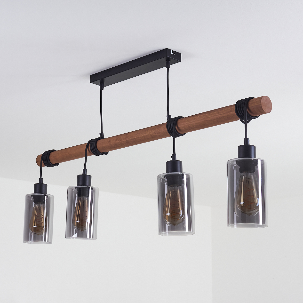 Eine moderne Deckenleuchte mit vier zylindrischen Glasschirmen, einem braunen Holzbalken, schwarzen Schnüren und einer weißen Decke.