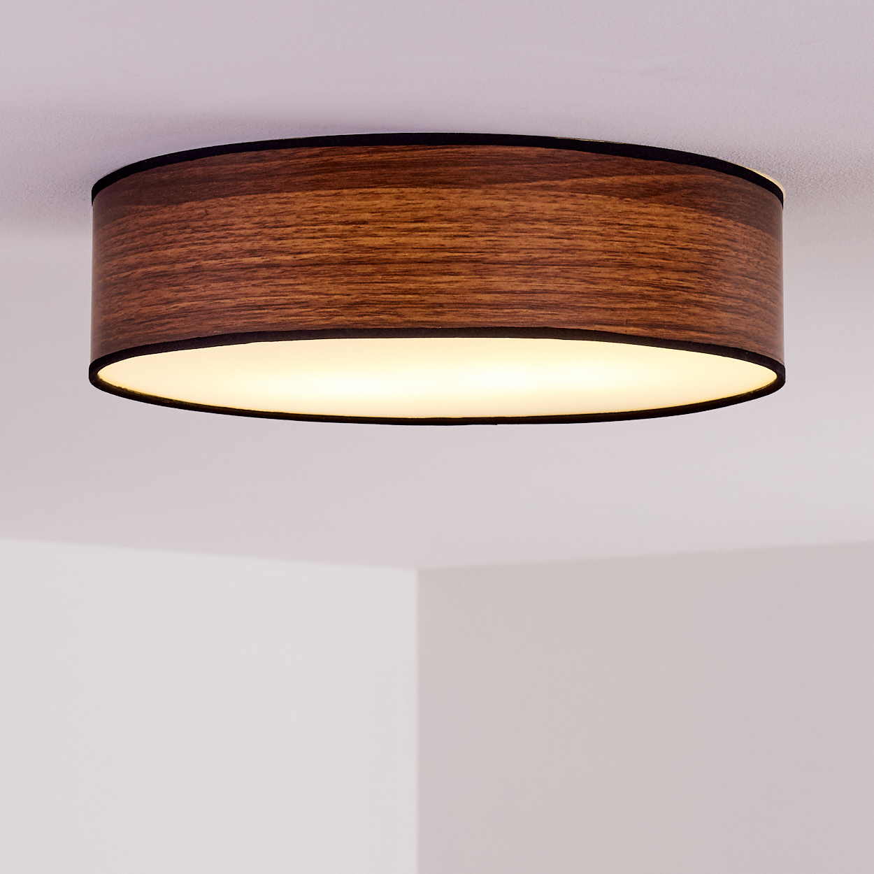 Eine Holzdeckenlampe mit schwarzem Rand ist im Bild zentriert. Die Lampe strahlt ein weiches, warmes Licht aus. Der Hintergrund ist weiß.