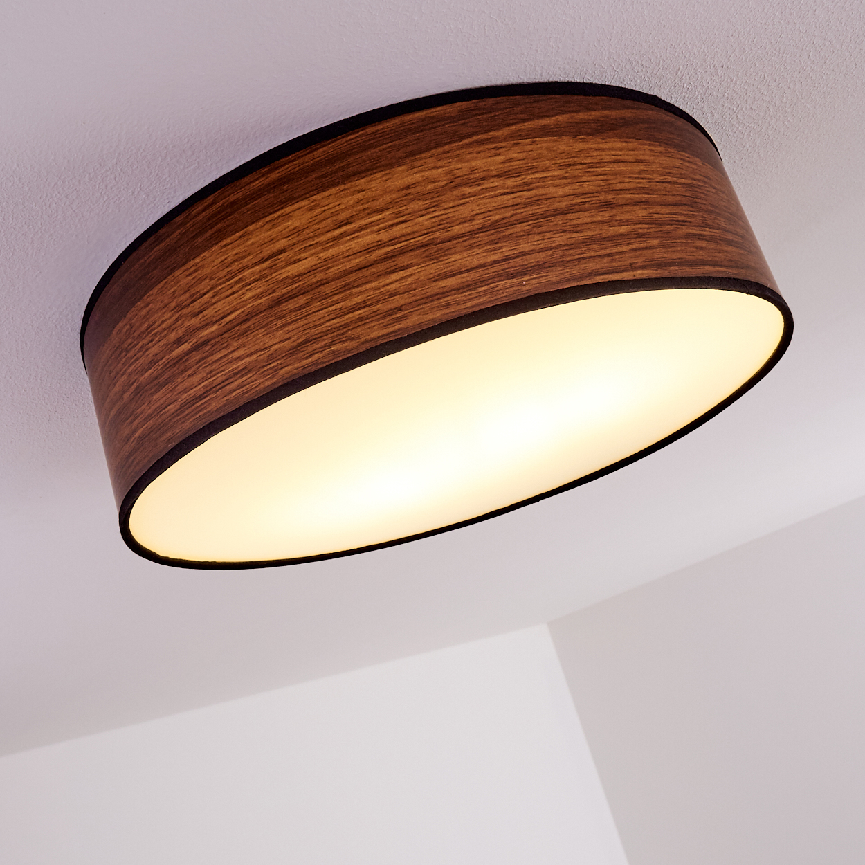 Eine Deckenlampe mit Holzschatten und schwarzer Verkleidung. Die Lampe ist oval und wird von innen beleuchtet. Weißer Hintergrund.
