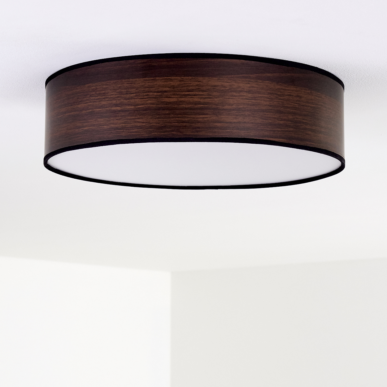 Eine Holzdeckenlampe mit dunkelbraunem Schirm und schwarzem Rand ist an einer weißen Decke befestigt. Die Lampe ist kreisförmig.