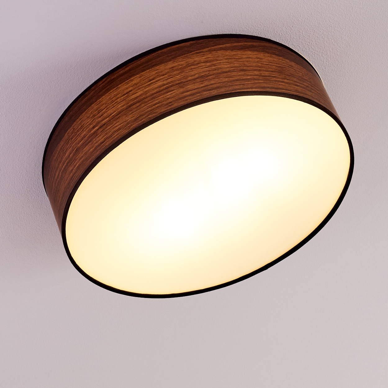 Eine Deckenleuchte mit Holzrahmen und hellem, ovalem Licht. Der Hintergrund ist eine schlichte weiße Decke.