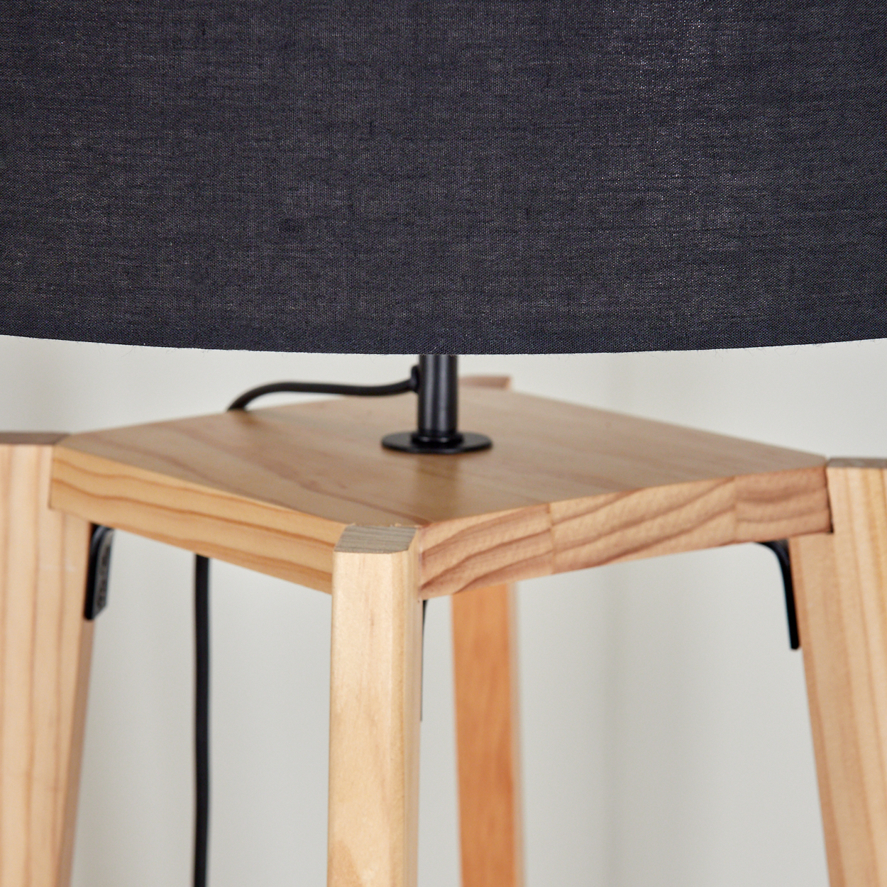 Nahaufnahme einer Lampe. Ein schwarzer Lampenschirm sitzt über einem Holztisch. Der Tisch hat vier Beine. Das Kabel der Lampe ist sichtbar.