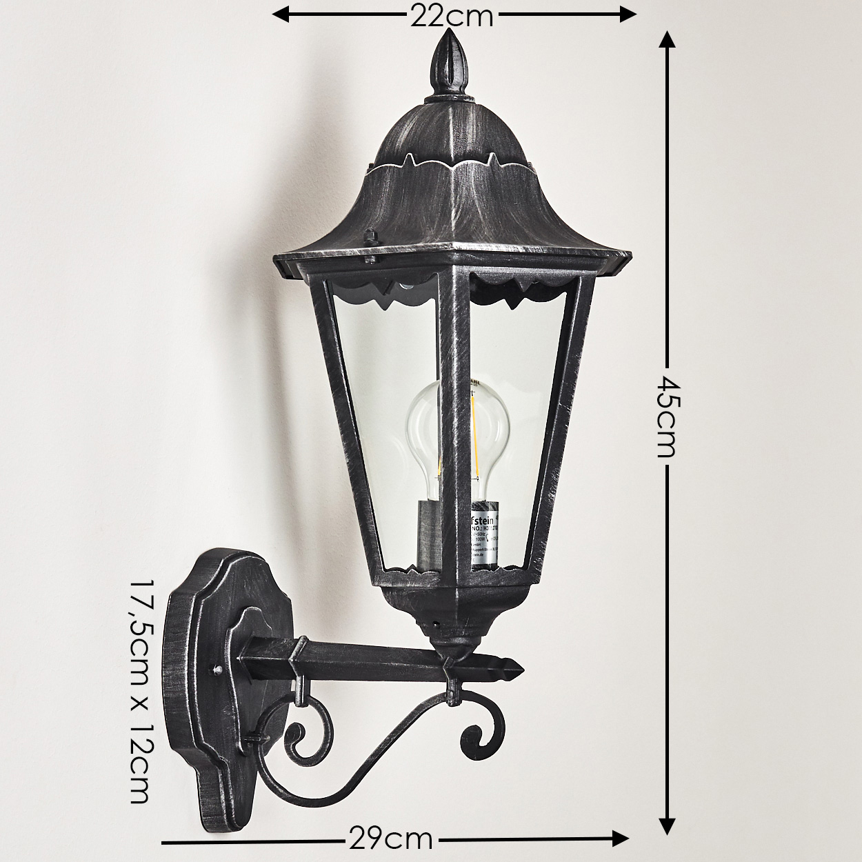 Eine wandmontierte, schwarze Außenlampe. Sie hat ein Glasgehäuse, eine Glühbirne und dekorative Metallarbeiten. Abmessungen sind angegeben.