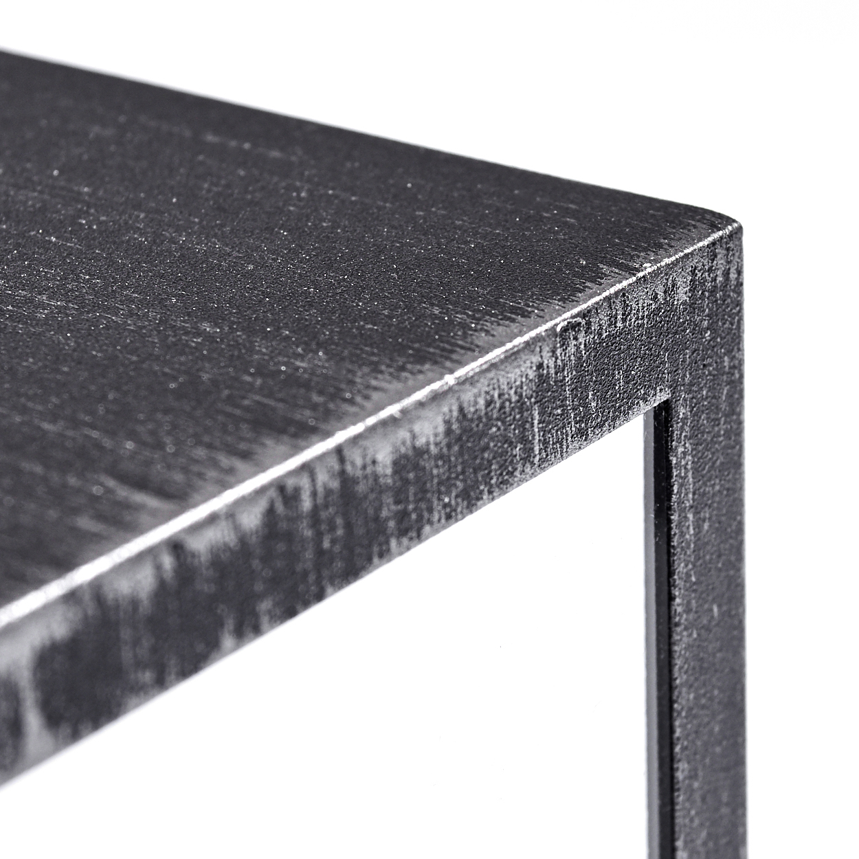 Nahaufnahme einer verwitterten, dunkelgrauen Metallecke. Die Oberfläche zeigt Textur, mit einem quadratischen Bein vor weißem Hintergrund.