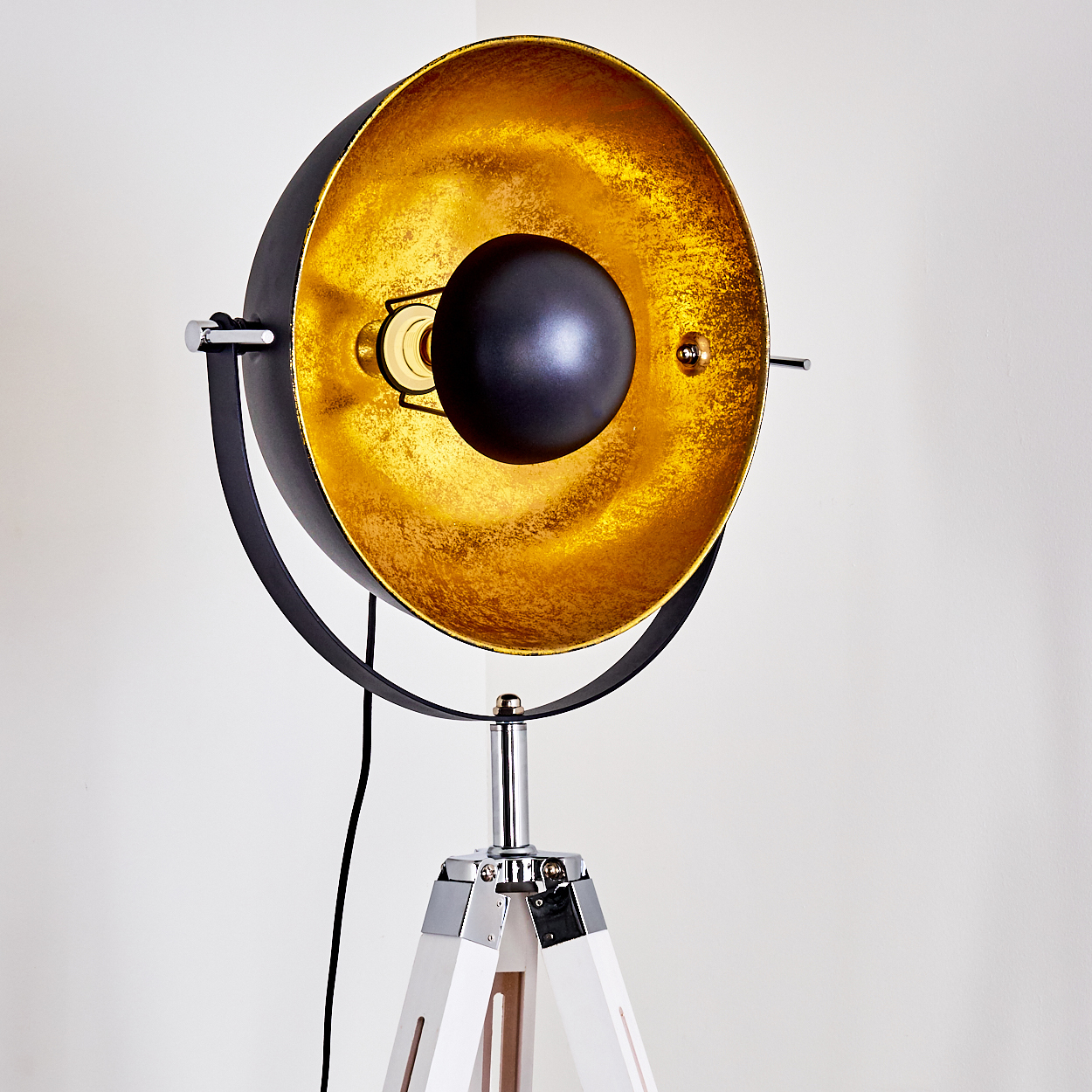 Eine schwarz-goldene Stehlampe. Die Lampe hat ein Stativ. Der Lampenschirm ist außen schwarz und innen goldfarben.