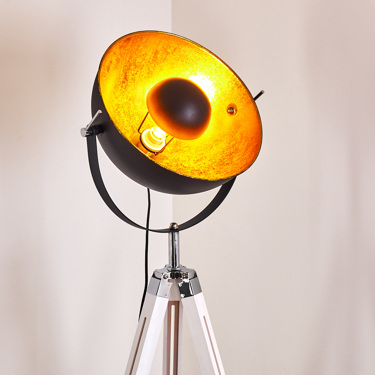 Eine schwarz-goldene Stehlampe mit weißem und silbernem Stativfuß. Die Lampe ist eingeschaltet und beleuchtet den Raum mit warmem Licht.