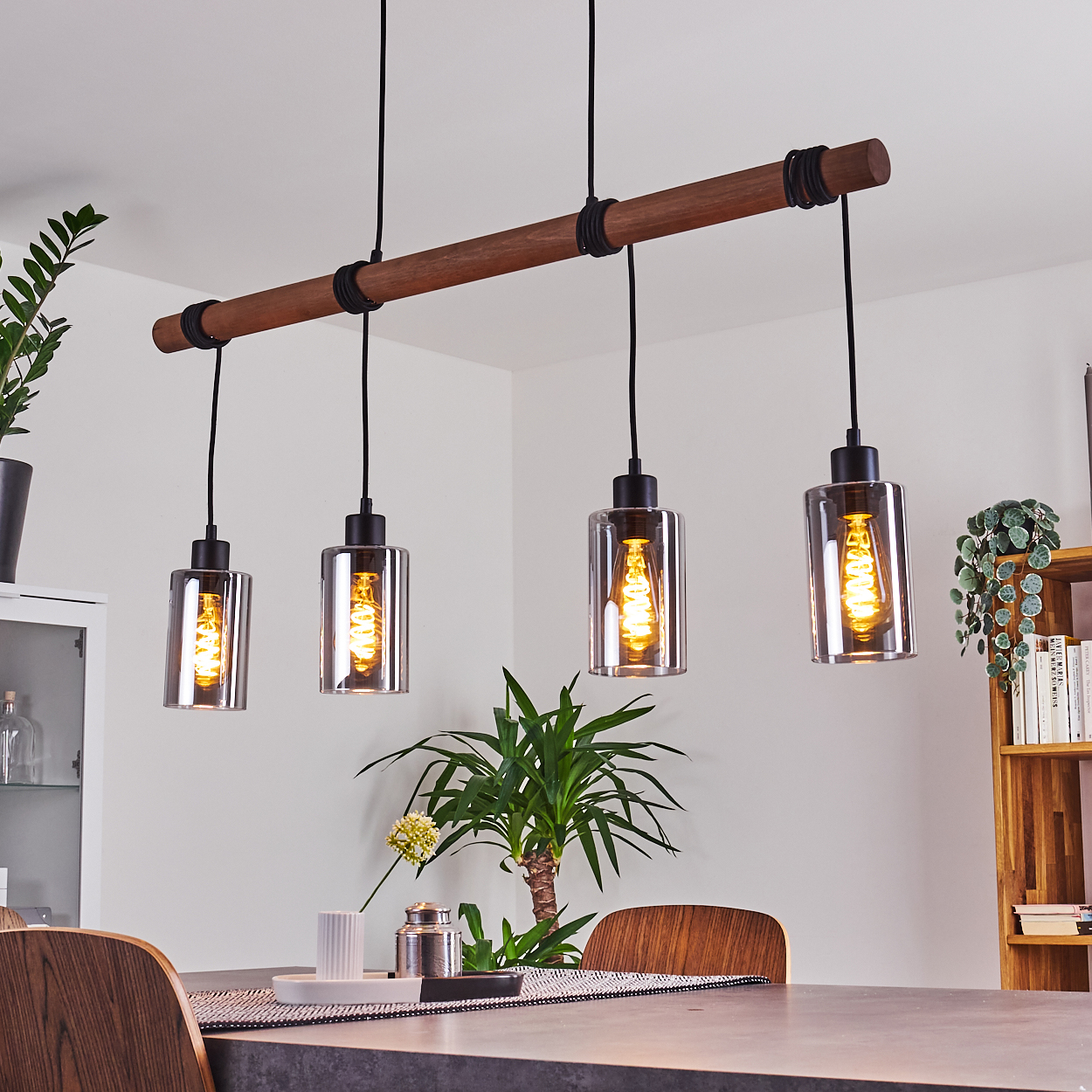 Ein Esszimmer mit Holztisch, vier Hängelampen mit Edison-Glühbirnen und Pflanzen.