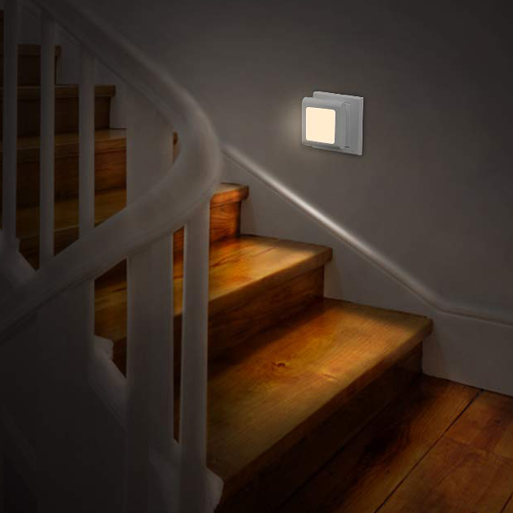 Holztreppe mit weißem Geländer und einer beleuchteten Wandleuchte. Warmes Licht beleuchtet die Stufen. Der Hintergrund ist dunkel.