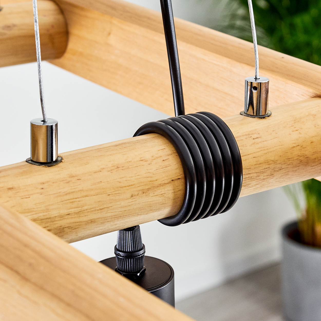 Nahaufnahme einer hölzernen Lampenhalterung. Helle Holzbalken, schwarze Metallringe und Akzente, Stahlkabel und eine dunkle Metallhalterung.