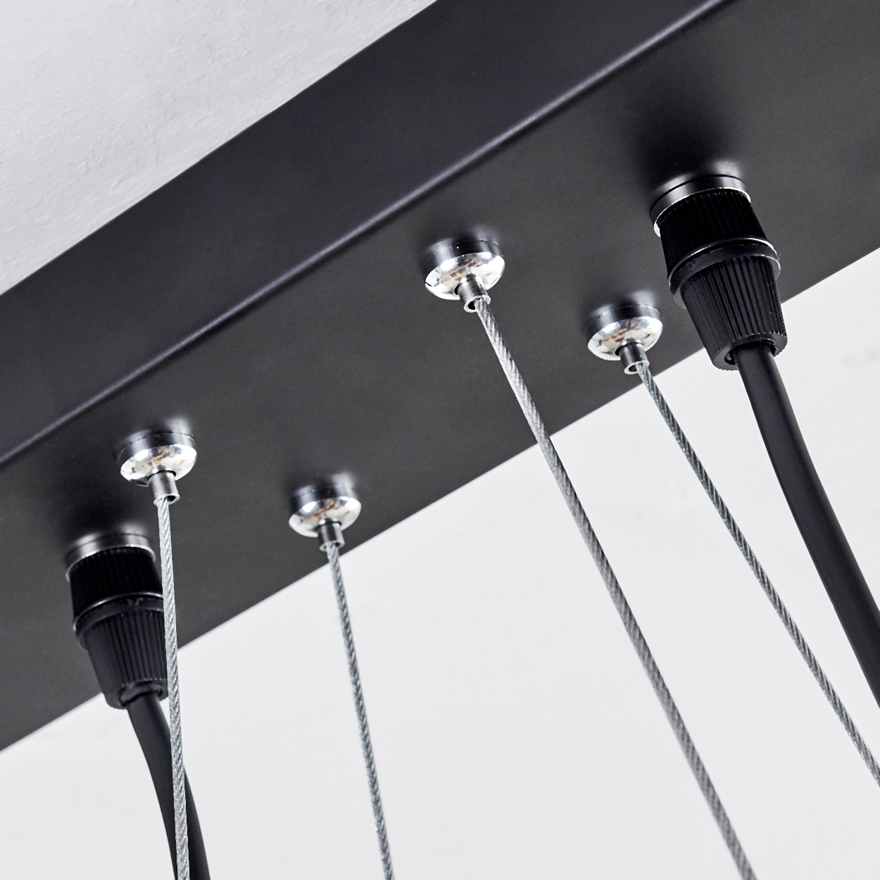 Nahaufnahme einer schwarzen Deckenleuchte. Kabel und Drähte hängen herunter. Metallbeschläge und eine weiße Decke sind sichtbar.