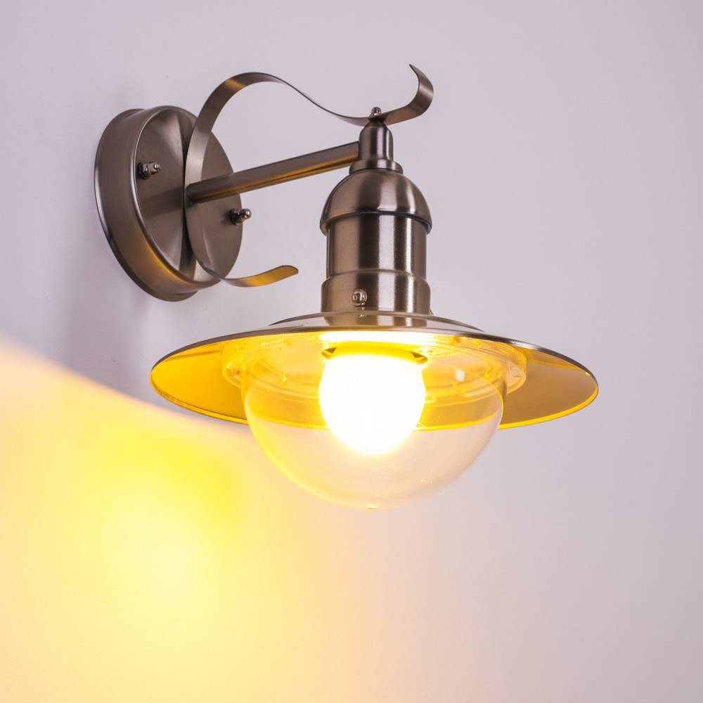 Eine Wandlampe mit Bronze-Finish. Die Lampe hat einen gebogenen Arm, einen gelb getönten Glasschirm und eine leuchtende Glühbirne.