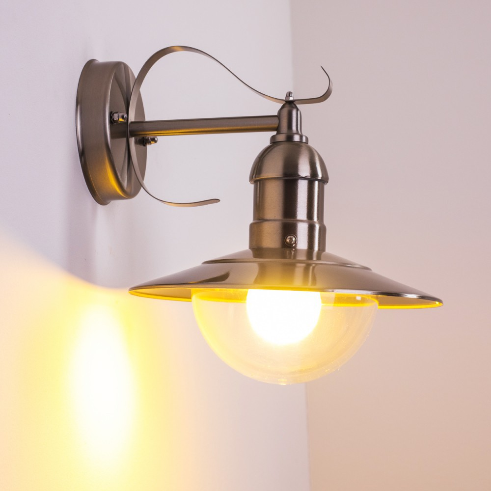 Eine metallische Wandlampe mit gebogenem Arm und Lampenschirm. Die Glühbirne leuchtet und wirft gelbes Licht an die Wand.