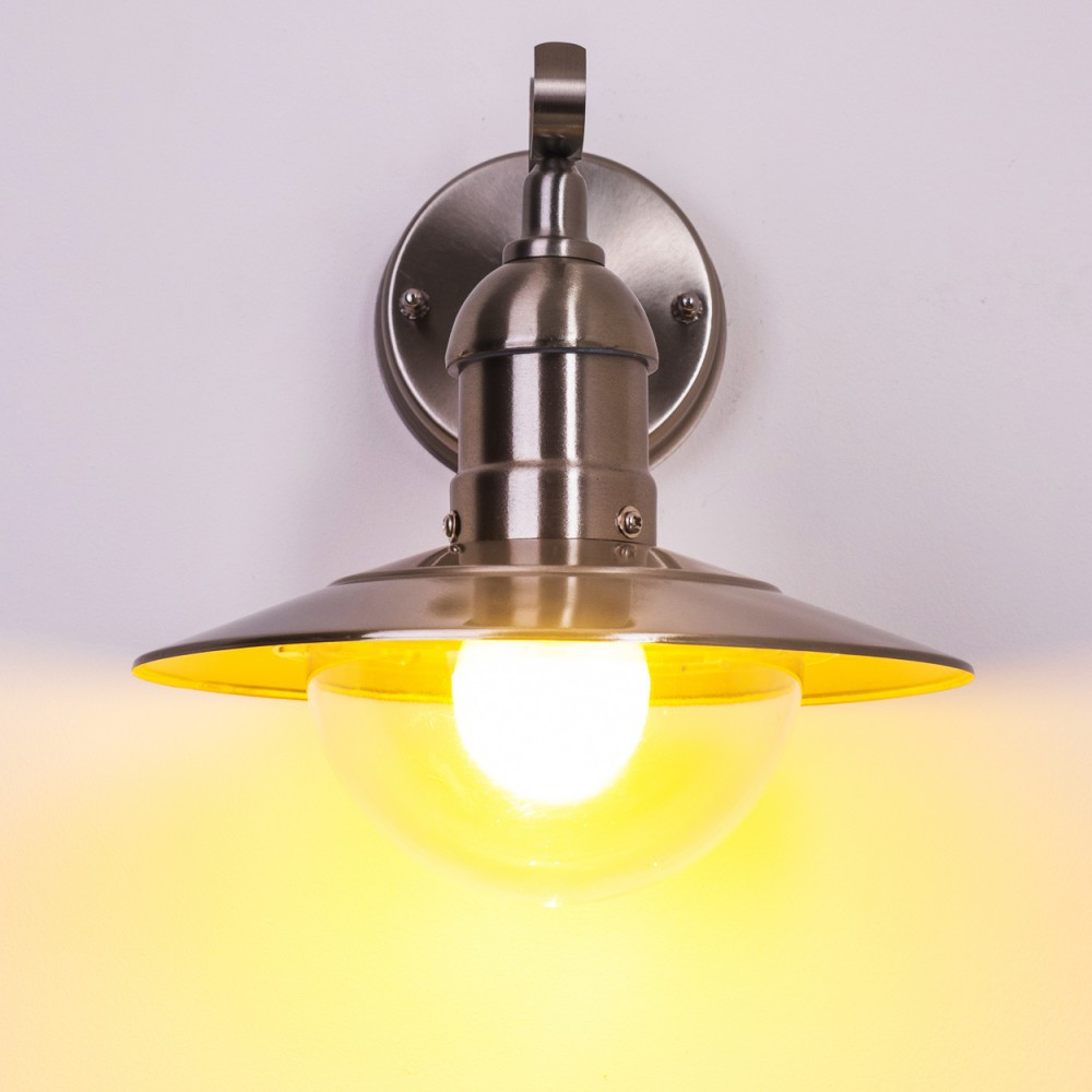 Eine Metall-Wandlampe mit Glasabdeckung. Sie hat ein gelbes Licht und ist an einer weißen Wand montiert.