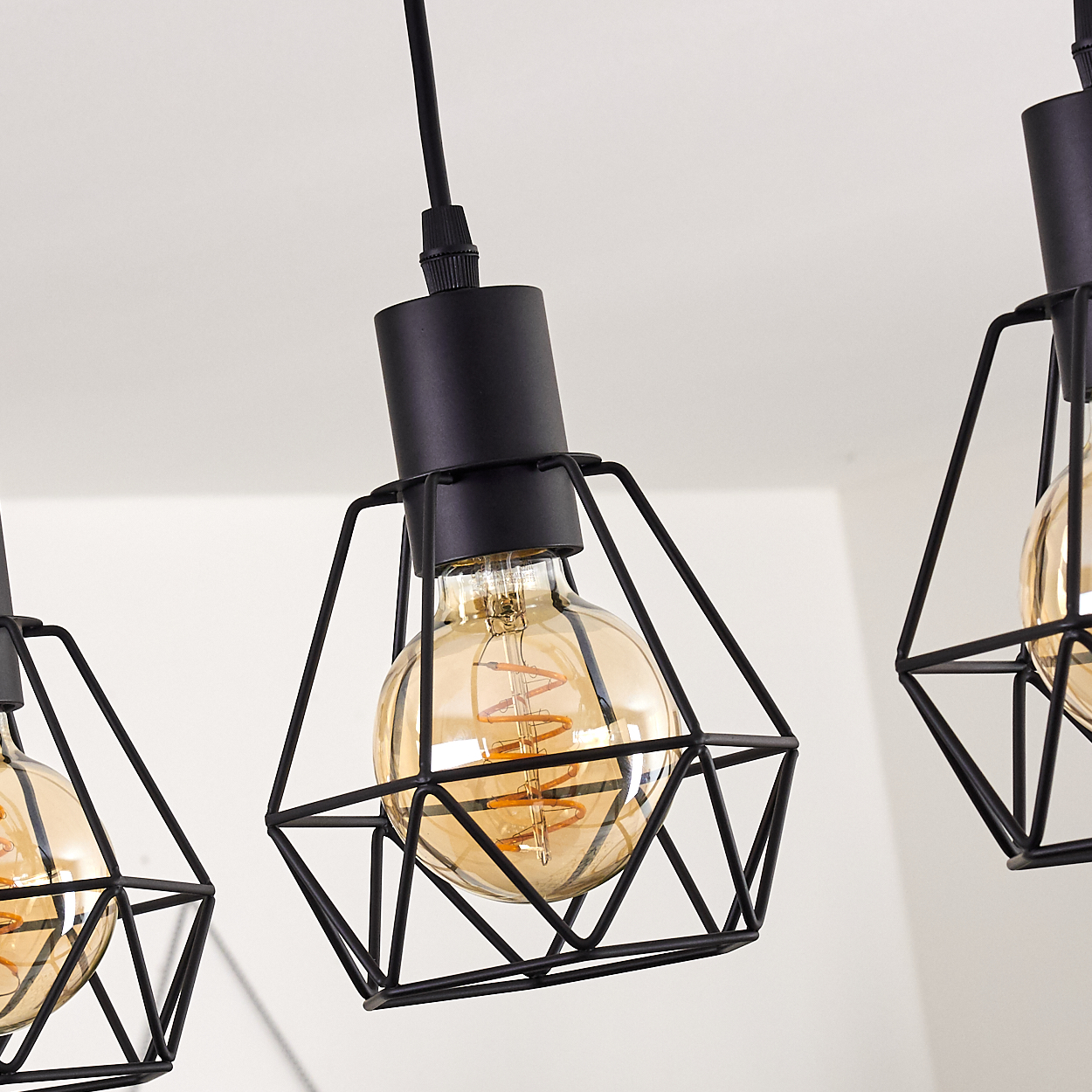 Nahaufnahme von drei schwarzen geometrischen Pendelleuchten mit Edison-Glühbirnen vor weißem Hintergrund.