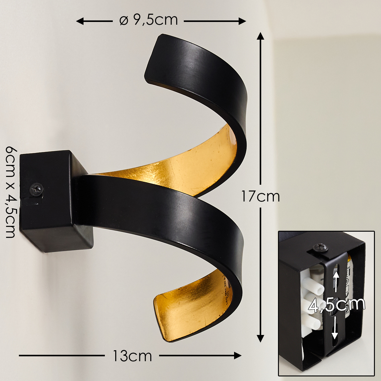 Schwarze und goldene Wandleuchte mit Spiraldesign. Abmessungen: 13cm x 17cm, Ø9,5cm. Die Lampe ist an einer weißen Wand montiert.
