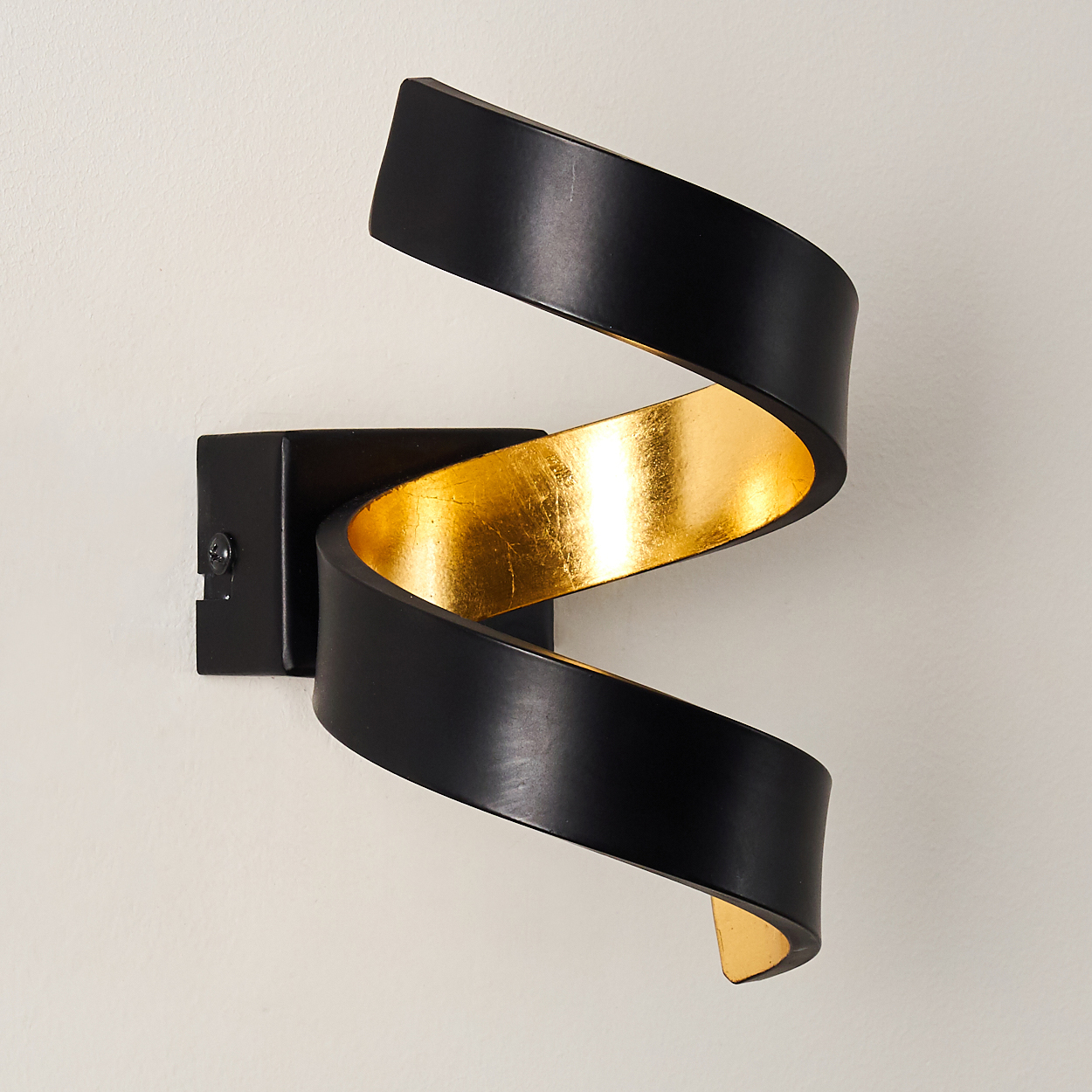 Eine moderne Wandleuchte. Schwarzes, gebogenes Metall mit goldfarbenem Innenraum. An einer Wand montiert, hat die Leuchte ein spiralförmiges Design.