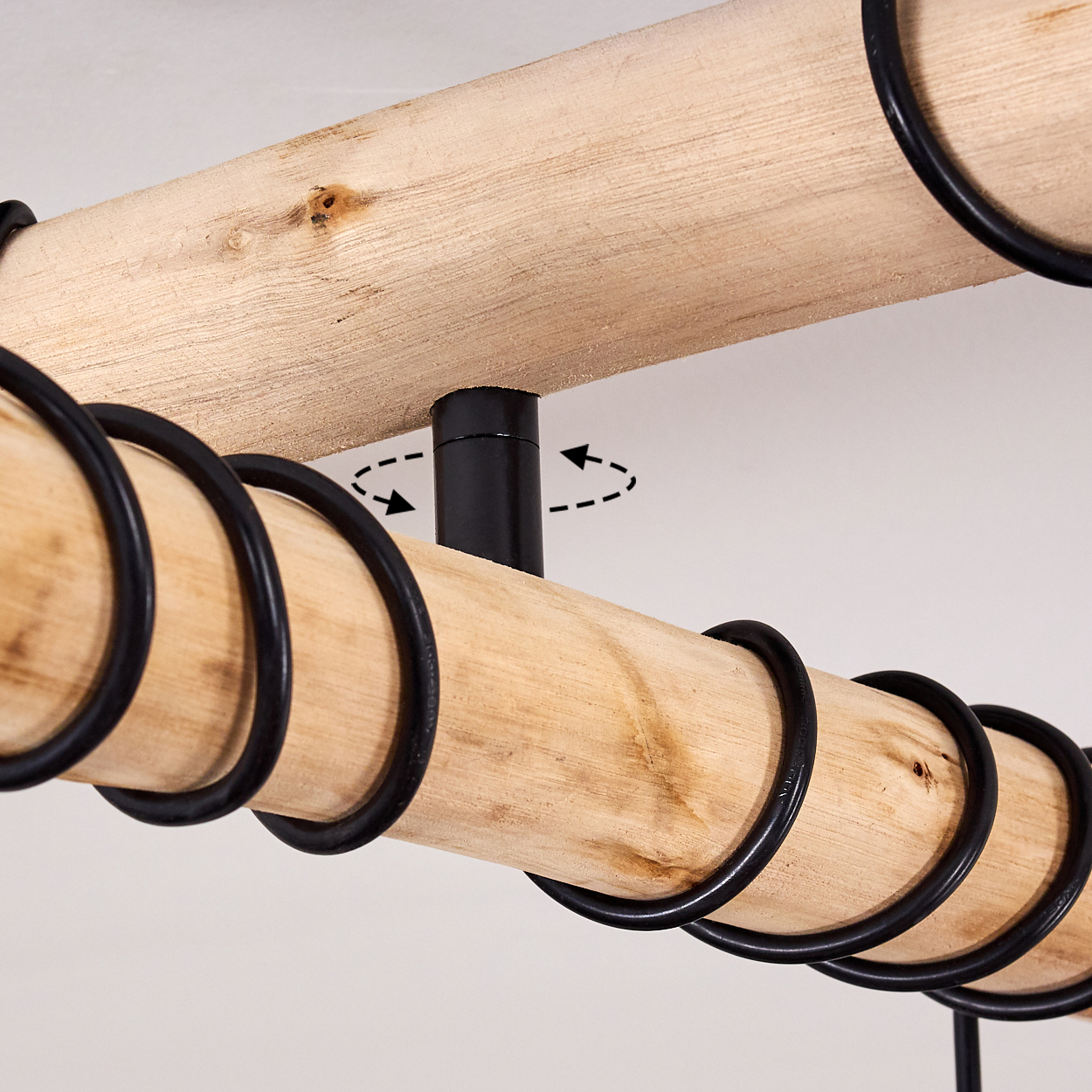Holzbalken mit schwarzen Metallringen und einer schwarzen Mittelstütze auf weißem Hintergrund, Pfeile zeigen die Drehung an.