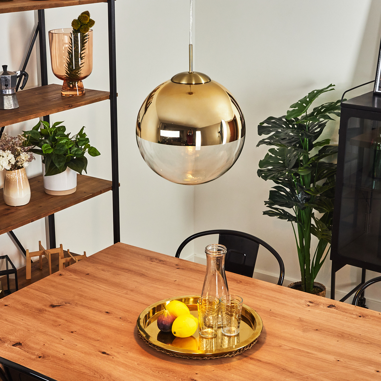Ein Esszimmer mit Holztisch, goldener Tablett mit Zitronen und Feigen. Eine goldene Glaslampe hängt darüber.