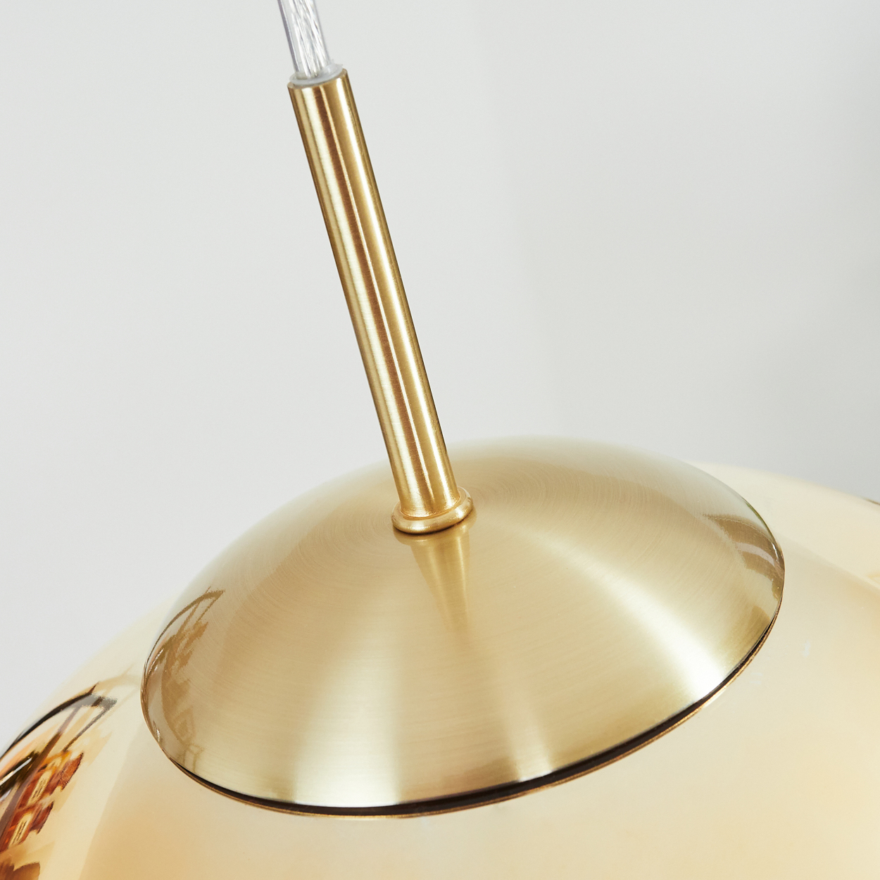 Nahaufnahme einer goldfarbenen Pendelleuchte. Die Lampe hat einen abgerundeten Schirm und eine Metallstange mit klarem Kabel.
