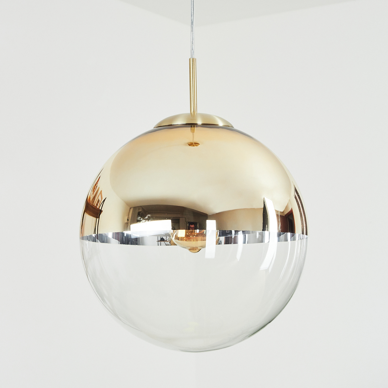 Eine kugelförmige Pendelleuchte. Die obere Hälfte ist goldfarben, reflektierend. Die untere Hälfte ist klar. Die Leuchte hängt von der Decke.