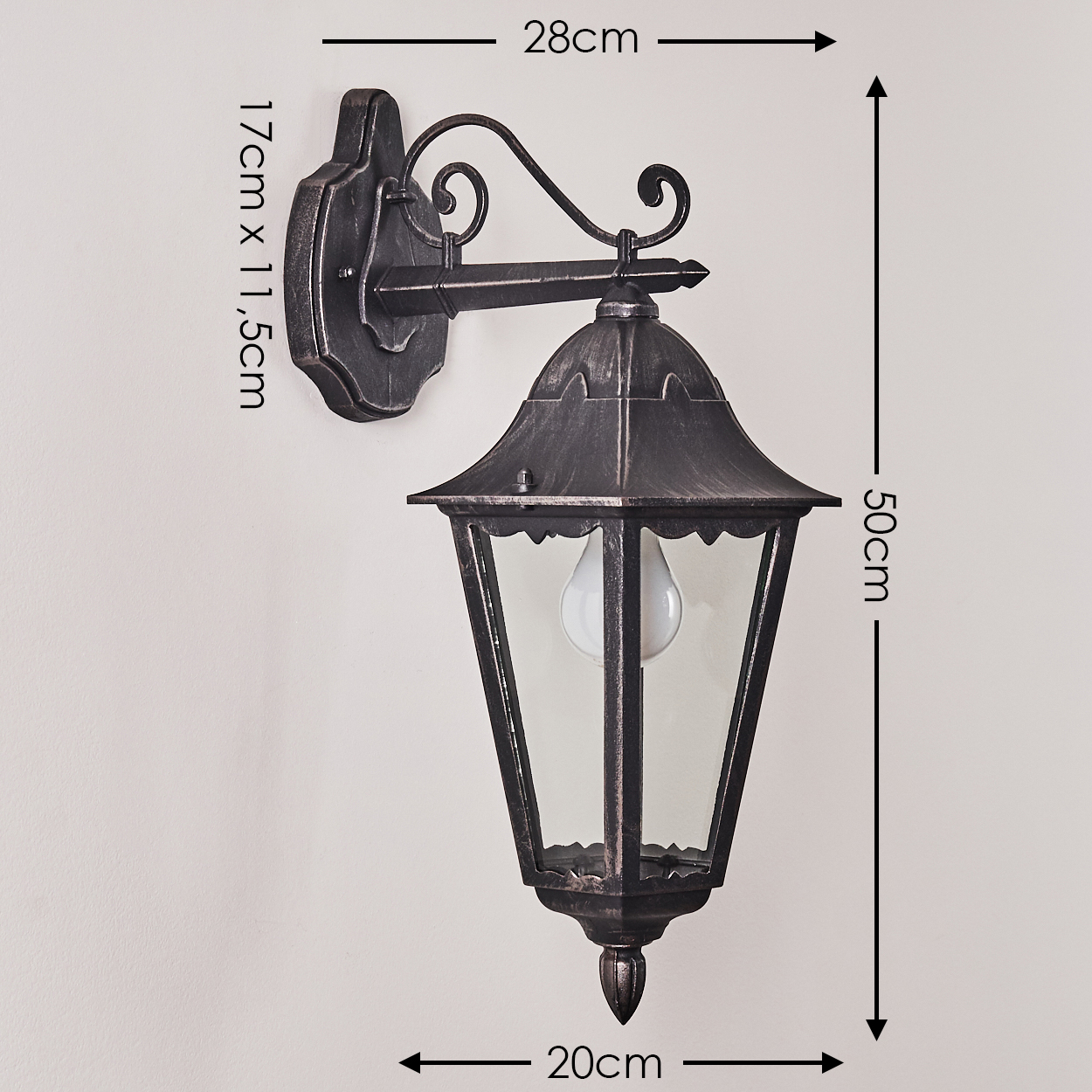 Eine antike bronzefarbene Wandlampe mit markierten Abmessungen. Sie hat ein glaseingeschlossenes Licht und dekorative Metallarbeiten, an einer weißen Wand montiert.