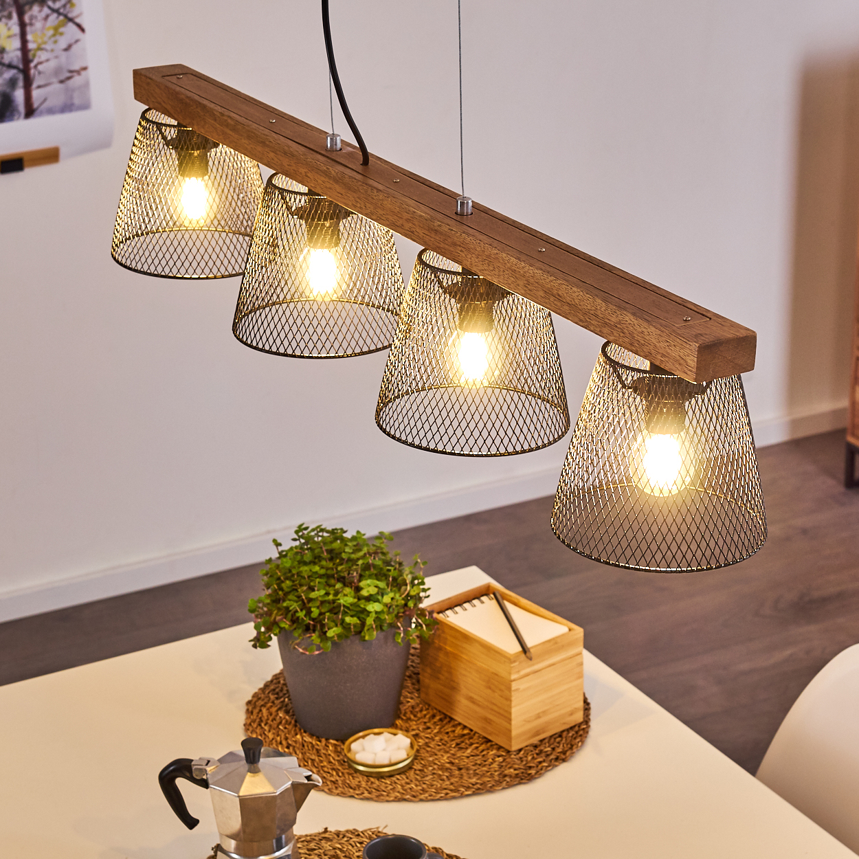 Ein Holzbalken mit vier Netzlampen hängt über einem Tisch mit einer Pflanze, einer Kaffeemaschine und einem Notizblock.