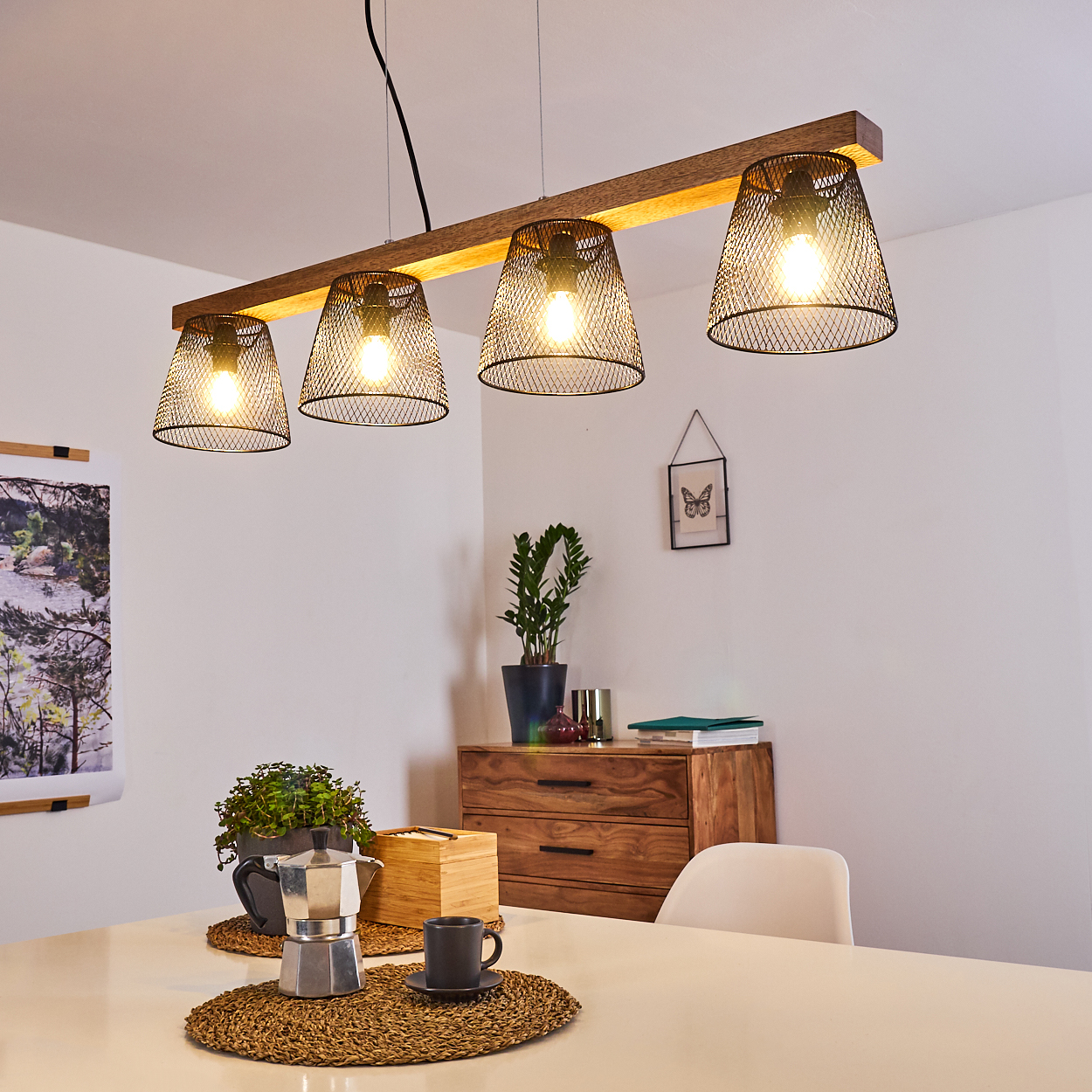 Ein modernes Esszimmer mit einem weißen Tisch, einer Kaffeemaschine und einer Holzlampe mit vier Lichtern. Im Hintergrund ein Holzschrank.