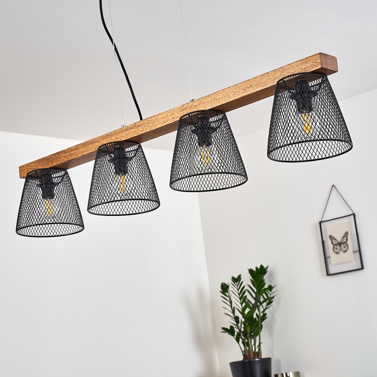 Ein Holzbalken mit vier schwarzen Netzlampen. Im Hintergrund stehen eine Pflanze und ein gerahmtes Schmetterlingsbild vor einer weißen Wand.