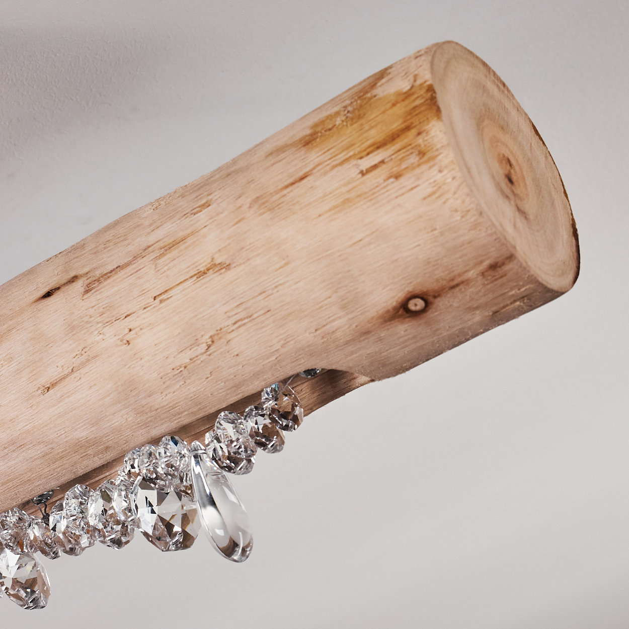 Ein Holzbalken mit daran hängenden Kristallen. Der Balken ist hellbraun. Der Hintergrund ist ein schlichtes Weiß.