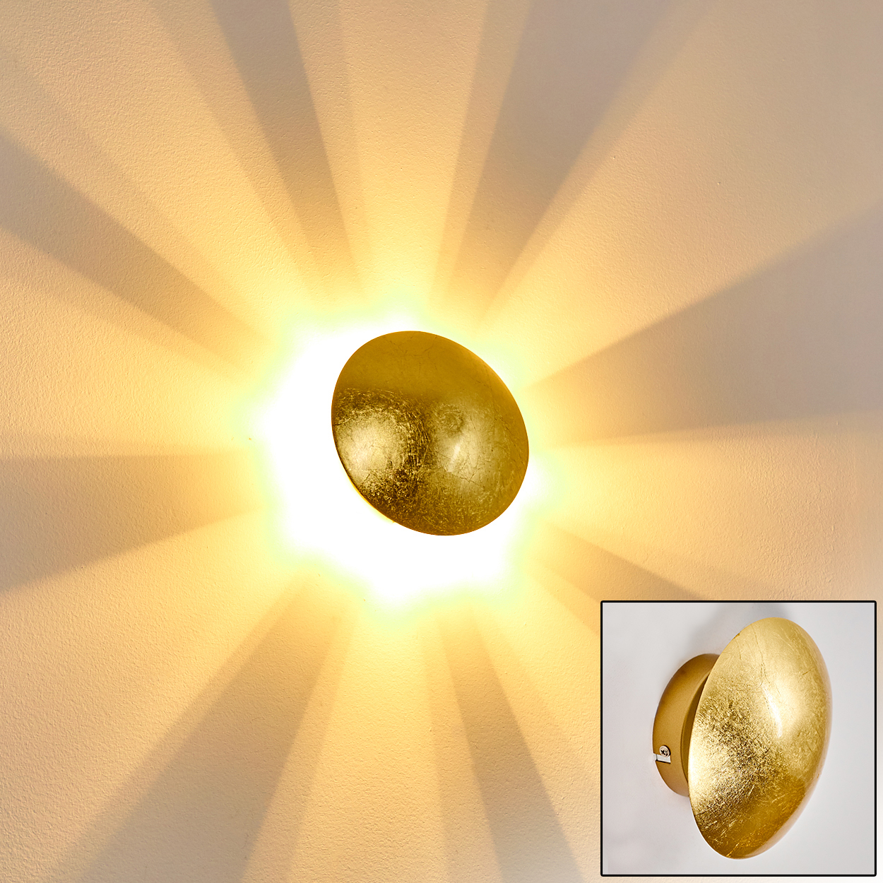 Eine goldene, ovale Wandleuchte wird beleuchtet und wirft Licht und Schatten auf eine weiße Wand. Eine kleinere Ansicht der Lampe befindet sich in der Ecke.