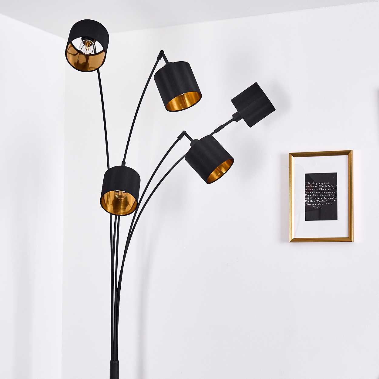 Eine schwarze Stehlampe mit fünf Lampenschirmen, goldfarbenem Innenraum. Ein gerahmtes Bild hängt an der weißen Wand. Die Lampe steht in der Ecke.