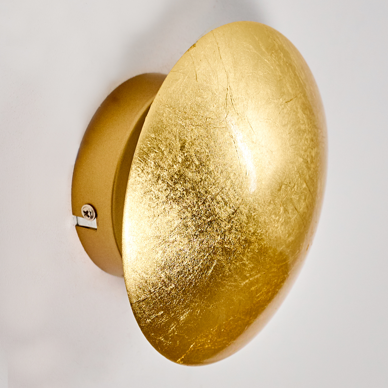Eine goldene Wandleuchte mit ovalem Schirm, vor einer weißen Wand. Die Lampe hat eine strukturierte, reflektierende Oberfläche.