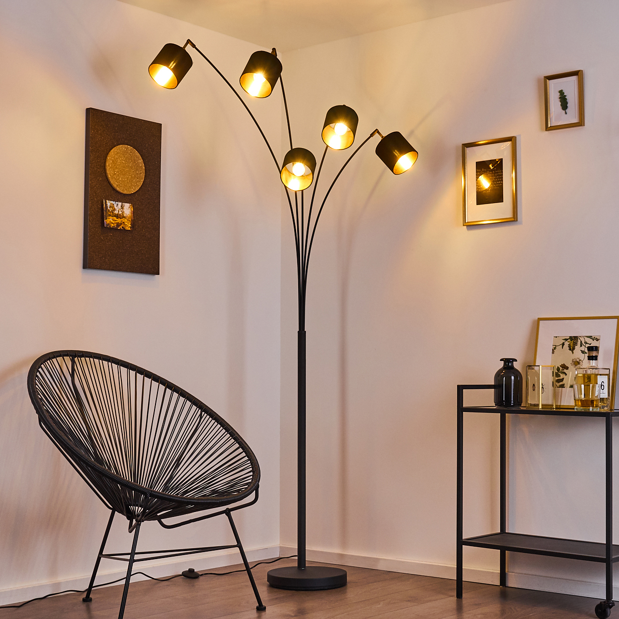 Ein modernes Wohnzimmer mit schwarzer Stehlampe, Stuhl und Beistelltisch. Bilder hängen an der Wand.