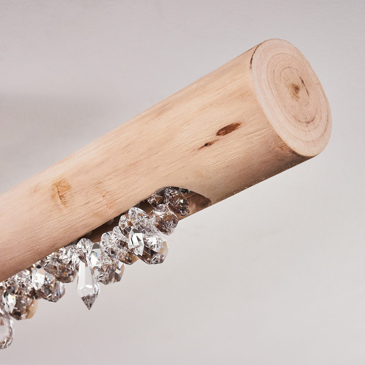 Ein Holzbalken mit eingebetteten Kristallen, die darunter hängen. Der Balken ist hellbraun, die Kristalle sind klar und facettiert. Weißer Hintergrund.