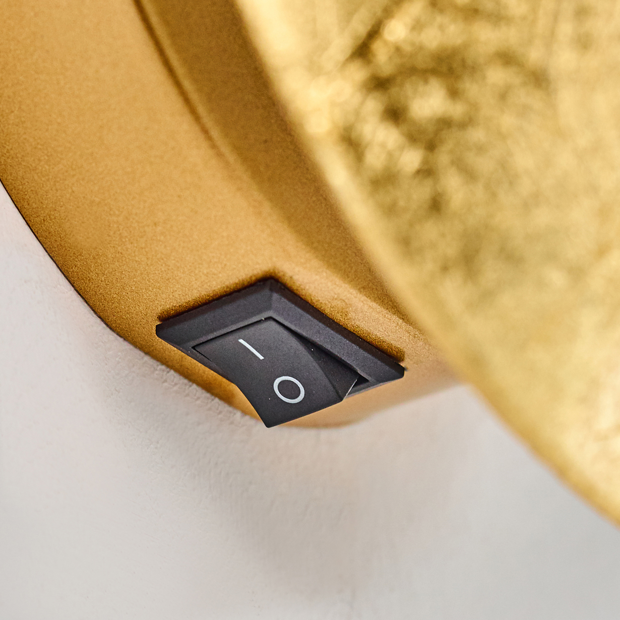 Ein schwarzer Ein/Aus-Schalter mit weißen Markierungen befindet sich auf einer goldfarbenen Oberfläche vor einem weißen Hintergrund.