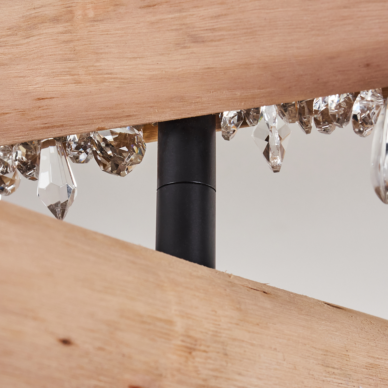 Nahaufnahme einer Lampe mit Holzbalken, schwarzem Pfosten und Kristallanhängern. Der Hintergrund ist schlicht weiß.