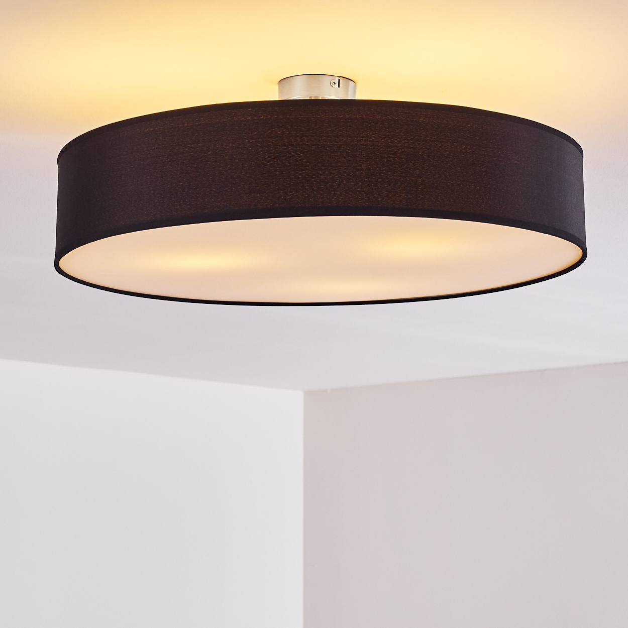 Eine schwarze, kreisförmige Deckenlampe mit weißem Innenraum ist an einer weißen Decke befestigt. Der Hintergrund zeigt weiße Wände.