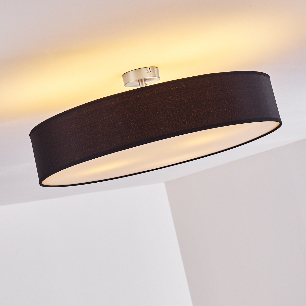 Eine schwarze, ovale Deckenlampe mit weißem Innenraum. Die Lampe ist an einer silbernen Halterung an der weißen Decke befestigt.