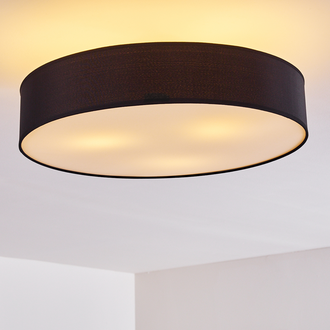 Eine schwarze, runde Deckenlampe mit weißer Unterseite ist an einer weißen Decke montiert. Die Lampe strahlt warmes Licht aus.