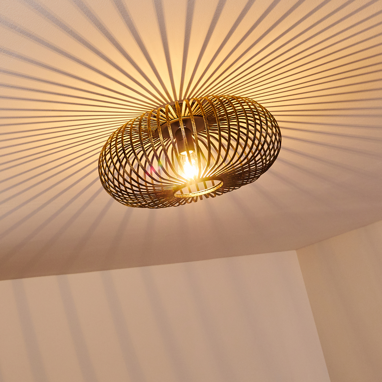 Eine moderne, ovale Deckenleuchte mit käfigartigem Design wirft radiale Schatten auf die Decke. Das Licht ist an und hell.
