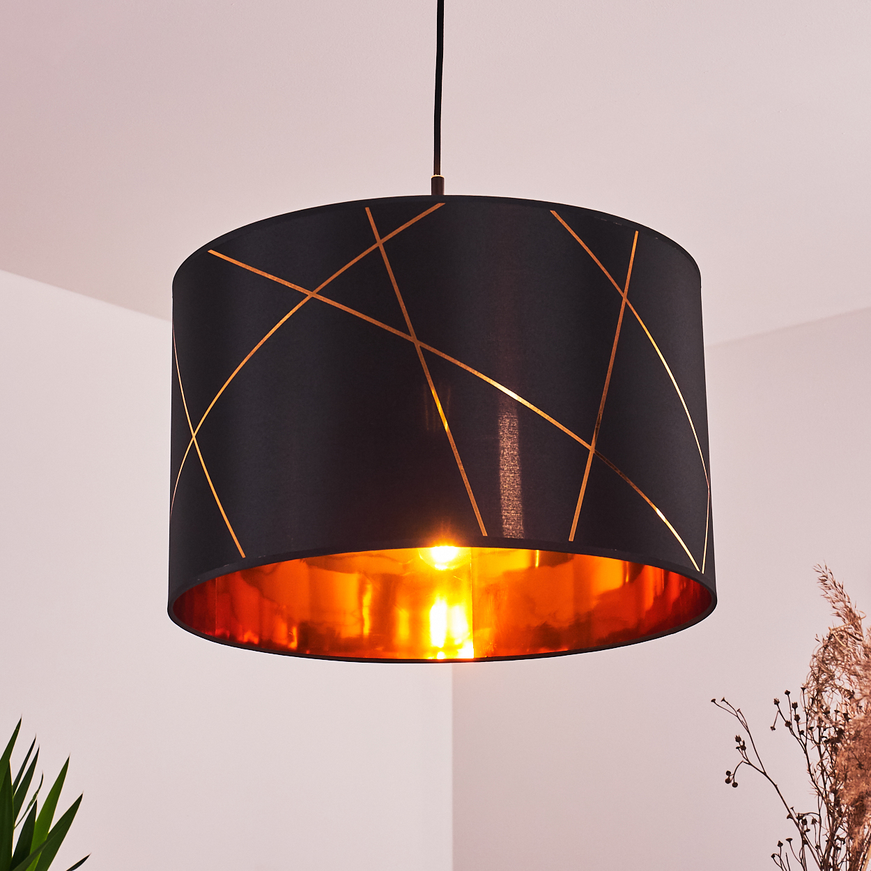 Ein schwarzer Lampenschirm mit Goldlinien hängt von der Decke. Die Innenseite ist goldfarben, und das Licht ist an und beleuchtet den Raum.