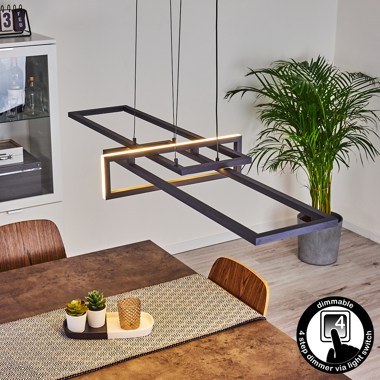 Ein modernes Esszimmer. Über einem Tisch hängt eine geometrische schwarze Leuchte. Im Hintergrund steht eine Pflanze in einem grauen Topf.