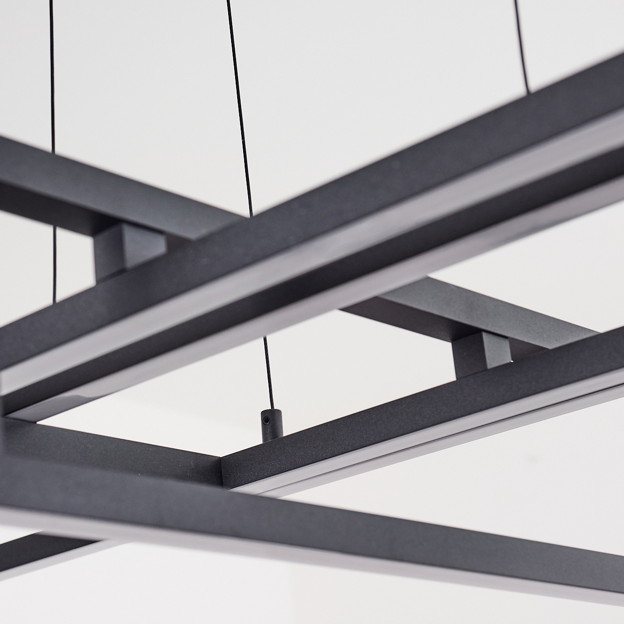 Nahaufnahme einer modernen, schwarzen, rechteckigen Deckenleuchte. Der Rahmen ist geometrisch, mit sichtbaren Drähten und weißem Hintergrund.