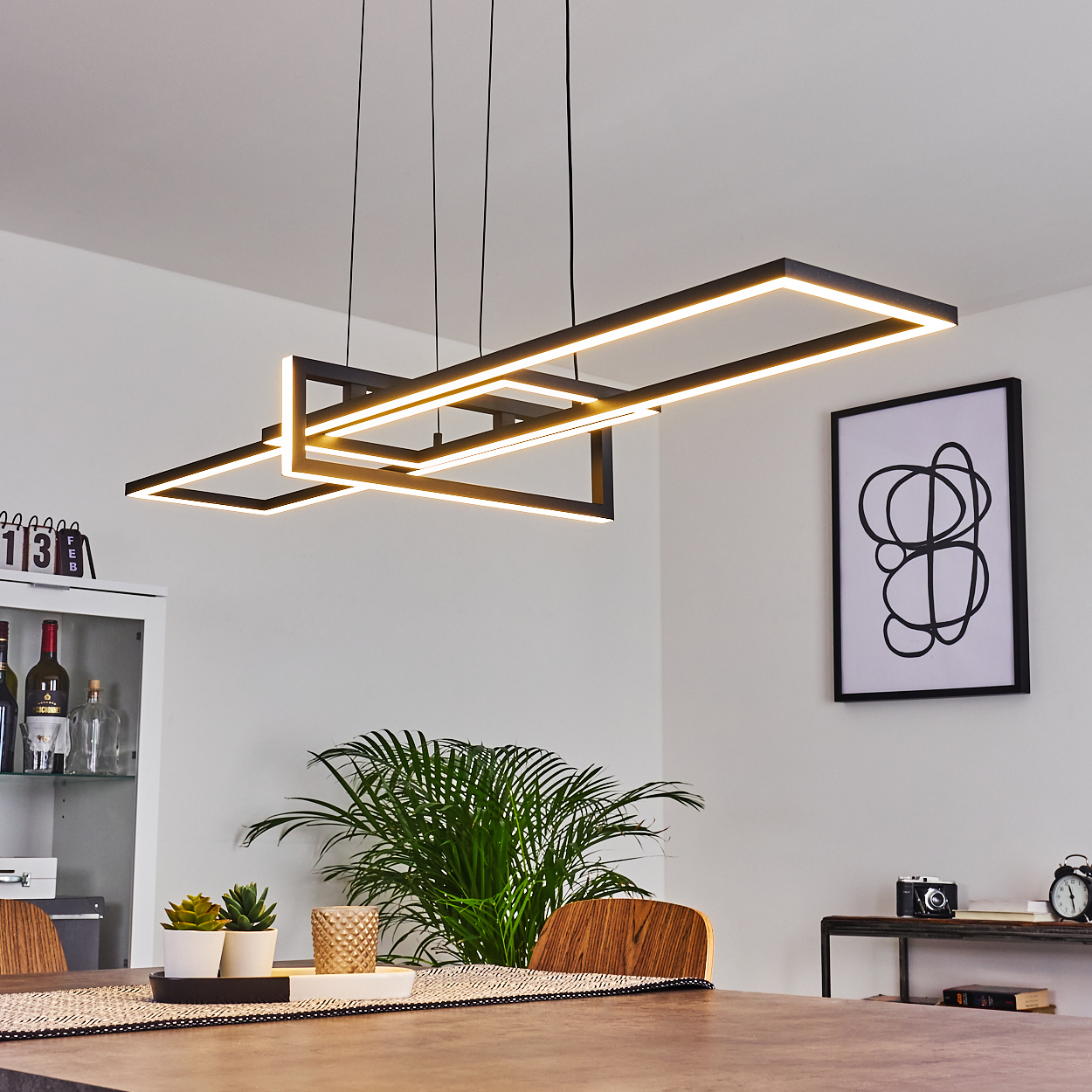 Ein modernes Esszimmer mit rechteckiger Leuchte. Pflanze, Kunstwerk und Tischdeko im Vordergrund.