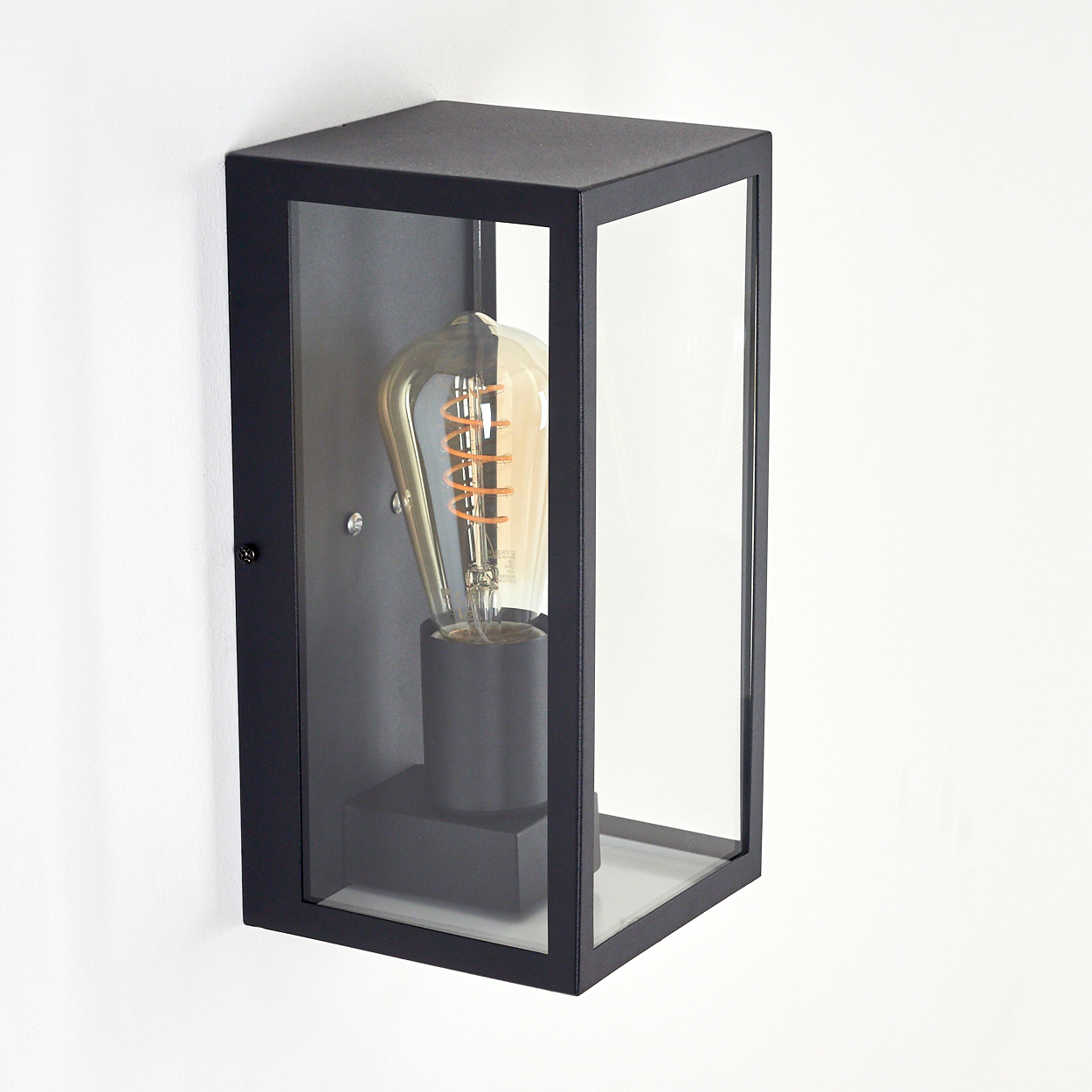 Schwarze rechteckige Außenlampe mit klarer Glasfront und Vintage-Glühbirne, an einer weißen Wand montiert.