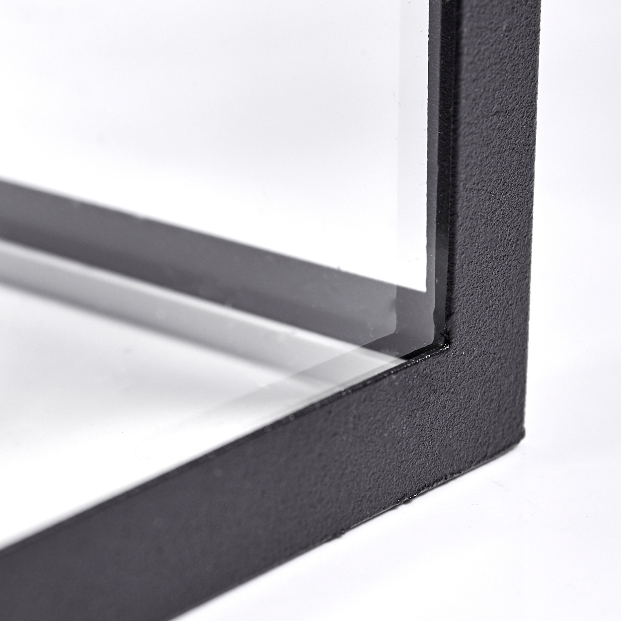 Nahaufnahme eines schwarzen, strukturierten Metallrahmens mit Glasscheiben. Der Rahmen befindet sich auf weißem Hintergrund, ist abgewinkelt und gut beleuchtet.