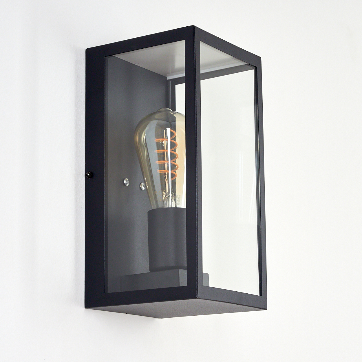 Eine schwarze Außenwandleuchte mit Glasscheiben und einer Glühbirne im Vintage-Stil, die an einer weißen Wand befestigt ist.