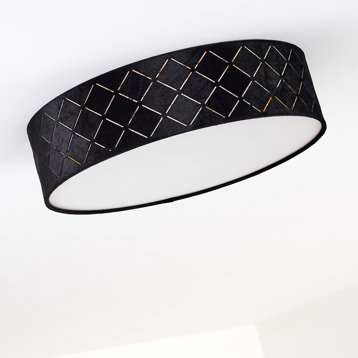 Schwarze Deckenlampe mit Diamantausschnitten. Weißer Innenraum reflektiert Licht. Vor weißer Decke.