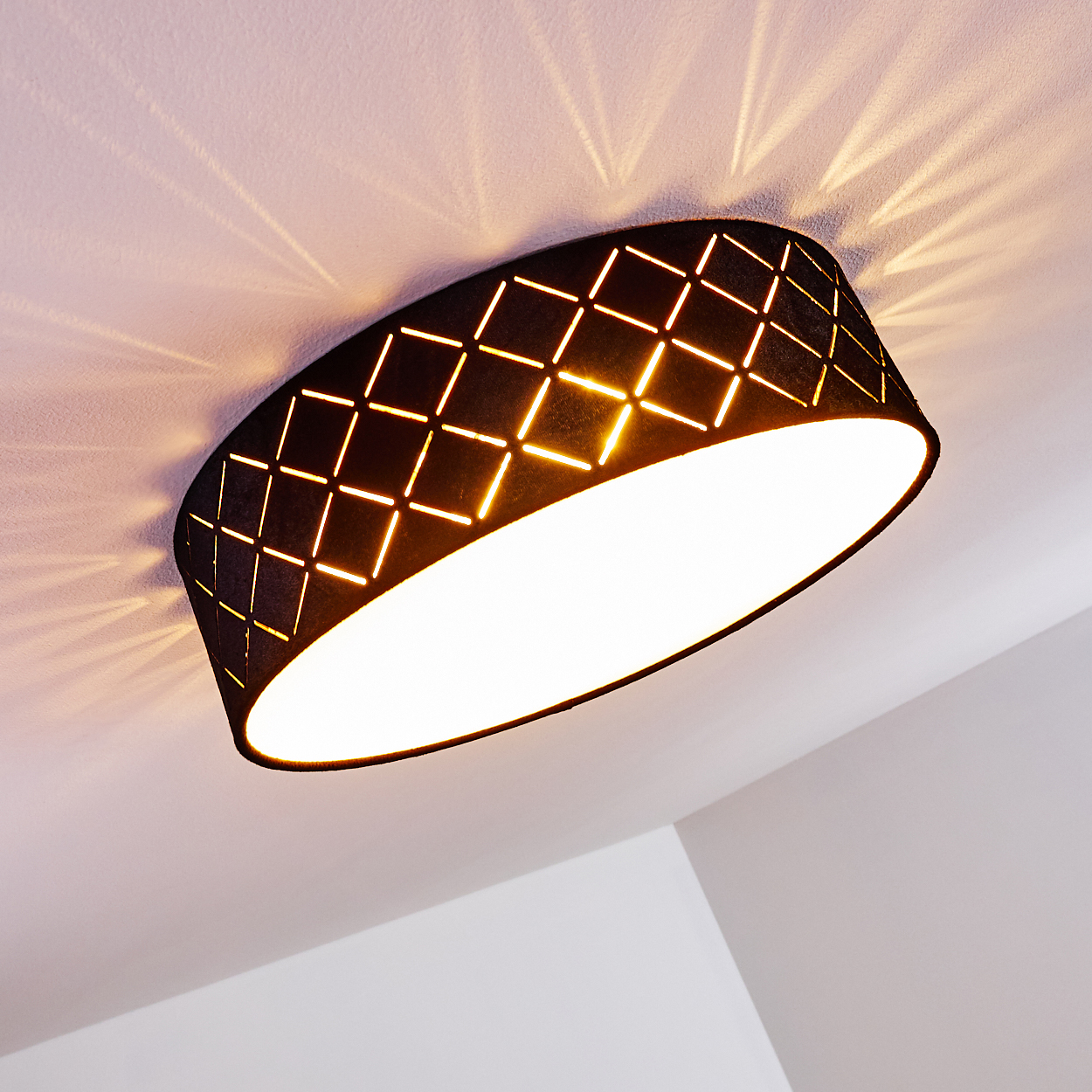 Eine schwarze Deckenlampe mit Rautenmuster. Licht scheint durch das Muster und wirft ein Muster auf die weiße Decke.