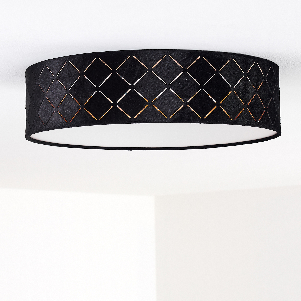 Schwarze Deckenlampe mit rautenförmigen Aussparungen. Weißer Innenraum und weißer Hintergrund.